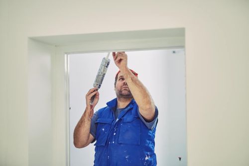 Worker using silicone for walls and door frame inside the house - renovation fixes.